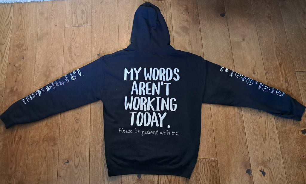 A black hoodie laid flat on a wooden floor, featuring white printed text on the back that reads 'MY WORDS AREN'T WORKING TODAY.' with smaller text below, and white graphic prints along both sleeves.