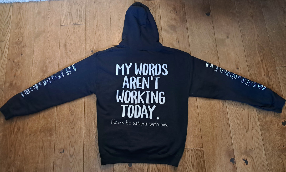 A black hoodie laid flat on a wooden floor, featuring white printed text on the back that reads 'MY WORDS AREN'T WORKING TODAY.' with smaller text below, and white graphic prints along both sleeves.