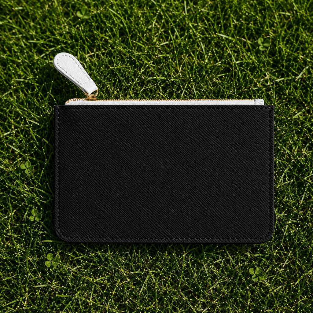 A small black textured zip pouch with a white pull tab and silver zipper, laid flat on green grass.