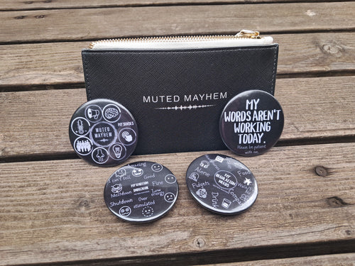 A black textured zip pouch with a gold zipper and the words 'MUTED MAYHEM' on the front, displayed on a wooden surface with four matching round black coasters featuring white text and doodles.