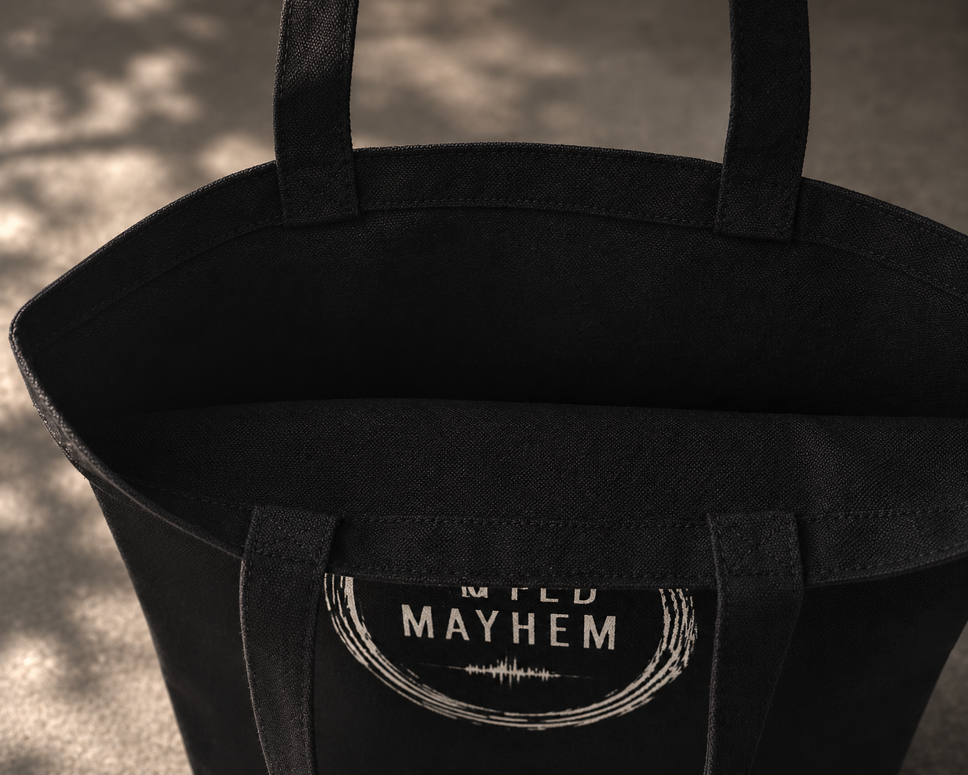 Black tote bag with 'Muted Mayhem' label on a textured surface promoting mental health and neurodivergence awareness by muted mayhem.