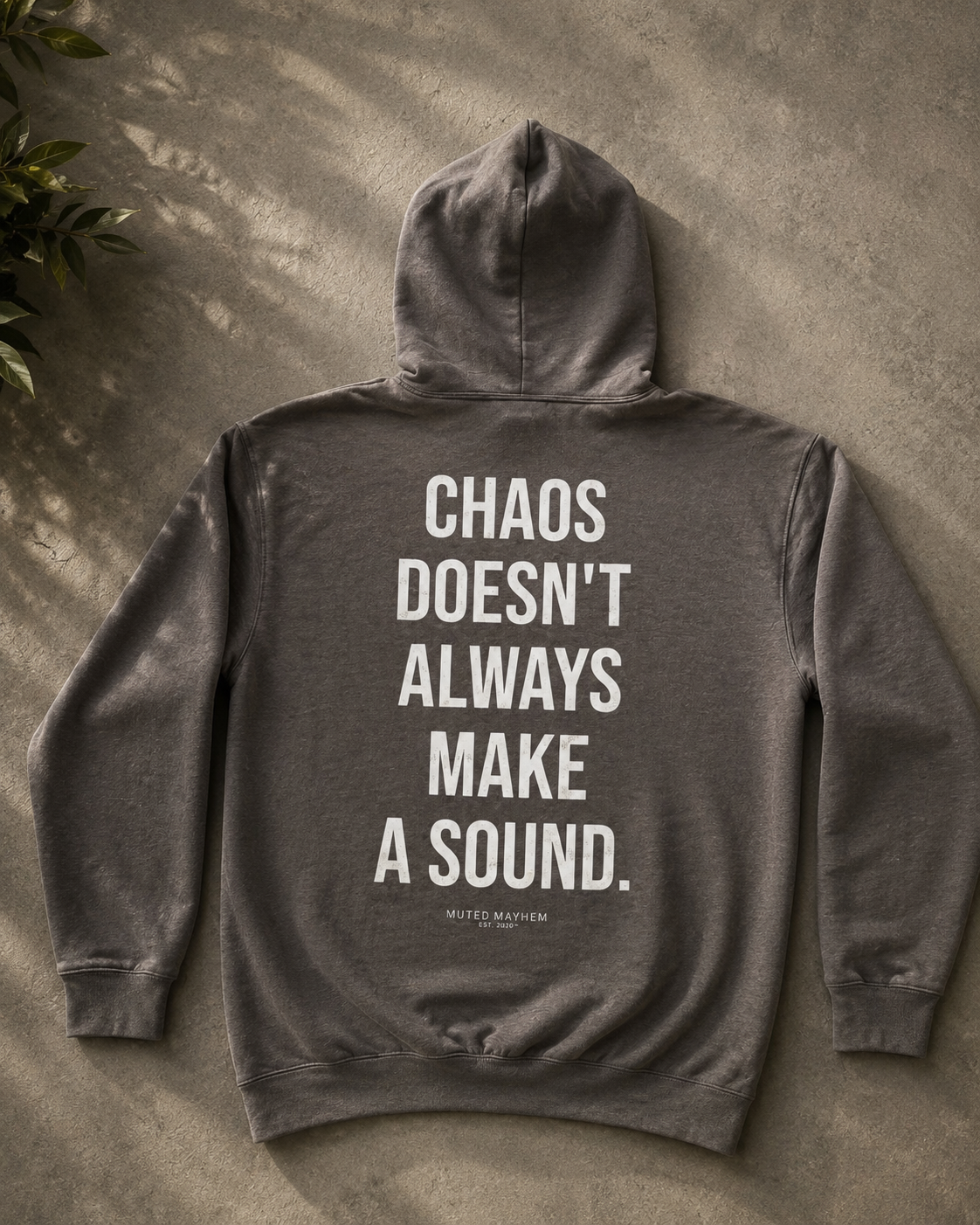 Gray hoodie with text 'Chaos doesn't always make a sound' on the back, placed on a textured surface. Promoting mental health and neurodivergence awareness by muted mayhem 