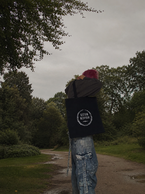 Person walking on a path with a bag over their shoulder in a forested area promoting mental health and neurodivergence awareness by muted mayhem.