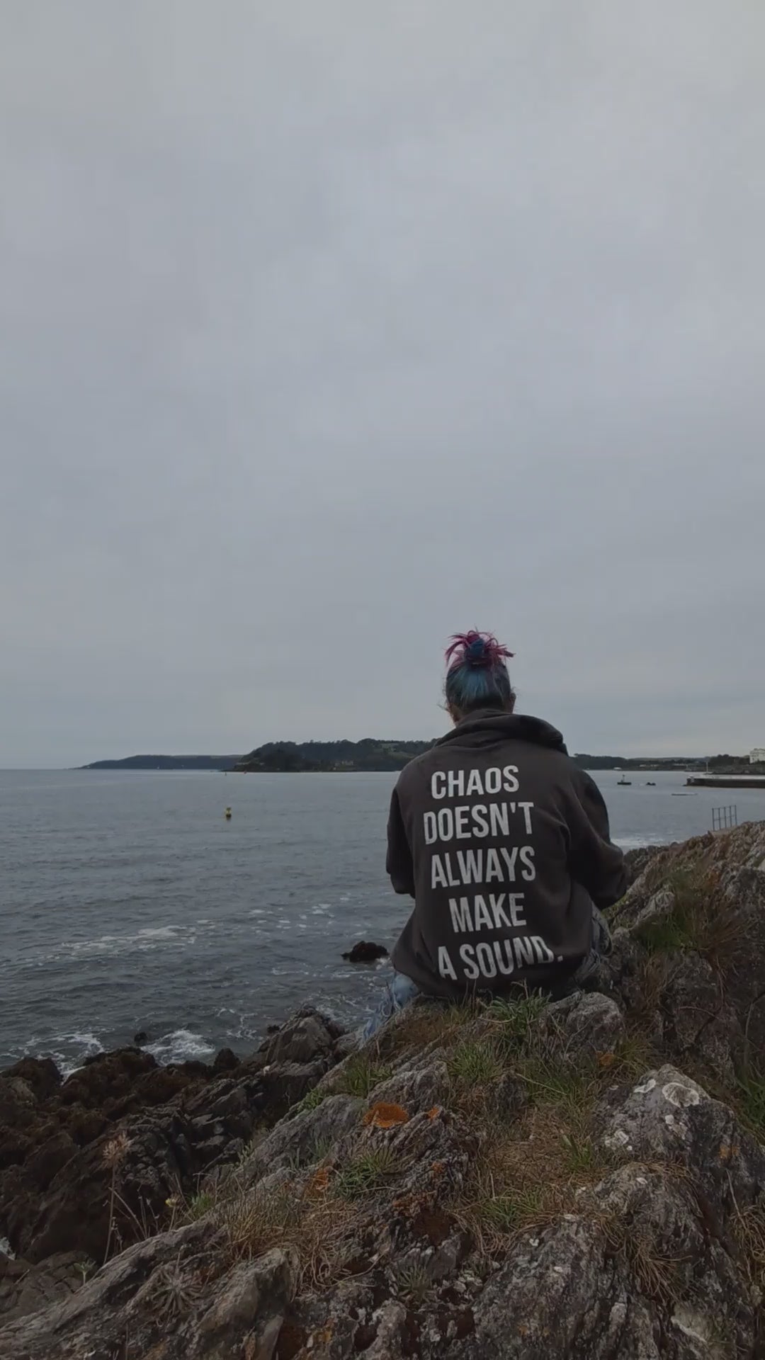 A short video on a women wearing a chaos doesn't always make a sound hoodie. While looking out at the see promoting mental health and neurodiversity.