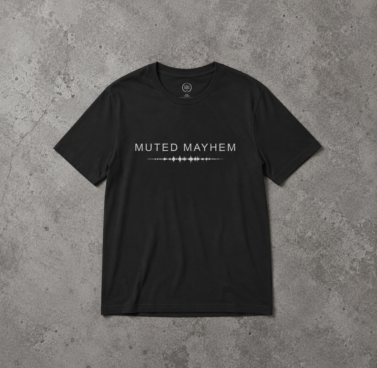 A black short-sleeve t-shirt with 'MUTED MAYHEM' and a soundwave graphic printed in white across the chest, laid flat on a textured gray concrete background promoting mental health and neurodivergence awareness by muted mayhem.