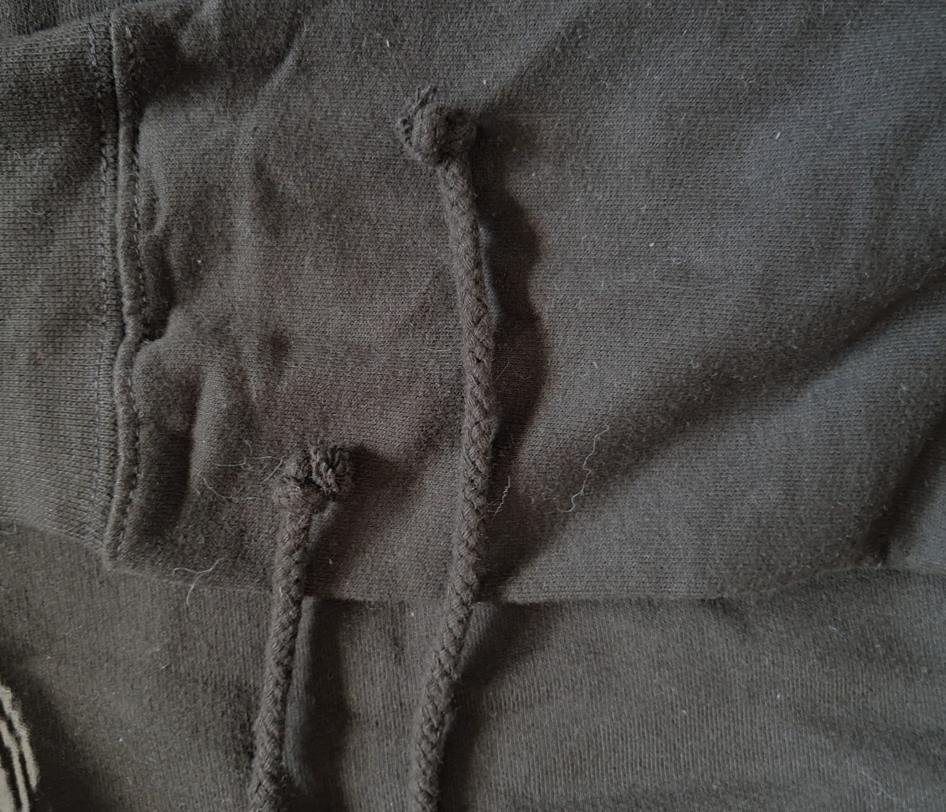 Close-up of a dark charcoal gray fabric with thick braided drawstrings knotted at the top promoting mental health and neurodivergence awareness by muted mayhem