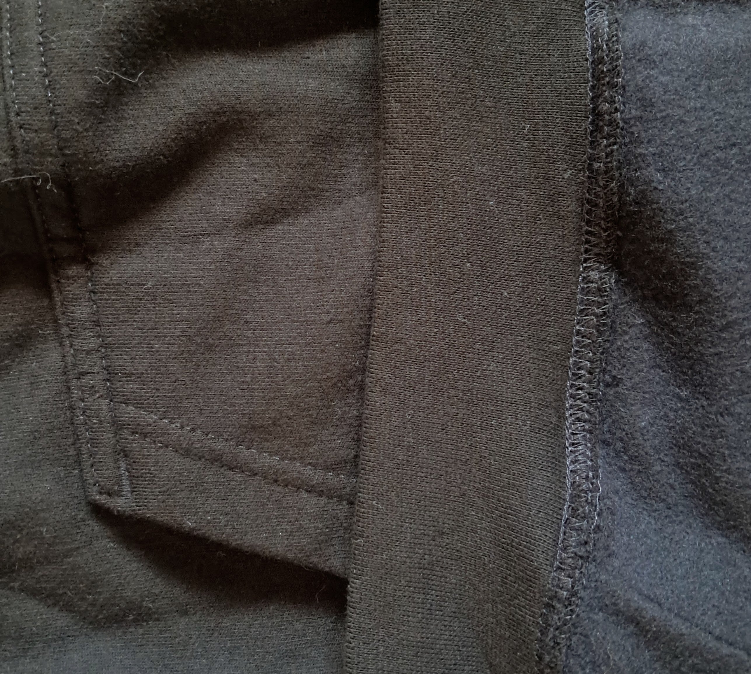 Close-up of dark gray fabric with a pocket seam and ribbed trim detail promoting mental health and neurodivergence awareness by muted mayhem
