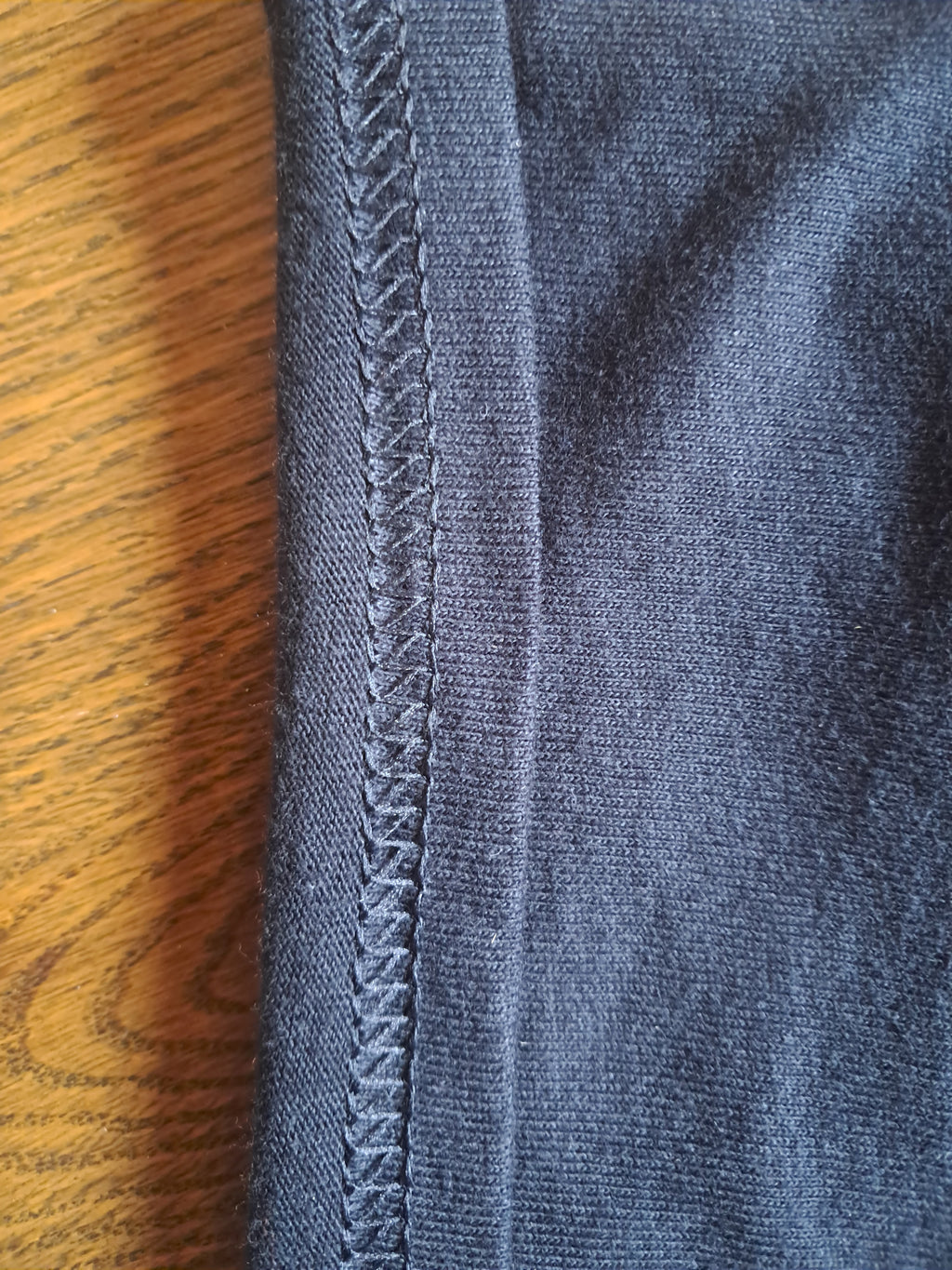 Close-up of a dark blue-gray ribbed knit fabric with a braided seam, placed on a wooden surface promoting mental health and neurodivergence awareness by muted mayhem.