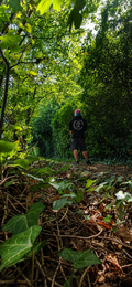 A women wearing a black hoodie with mental health awareness quote  on the back stands on a leaf-covered path in a dense green forest promoting mental health and neurodivergence awareness by muted mayhem