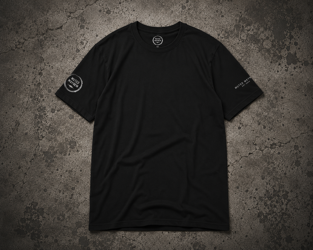 A black short-sleeve crewneck t-shirt with white printed graphics on the left sleeve and right chest, laid flat on a textured gray concrete background promoting mental health and neurodivergence awareness by muted mayhem.
