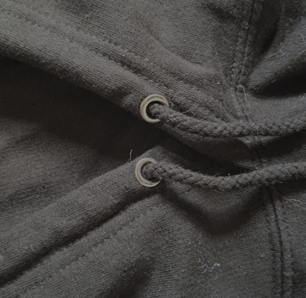 Close-up of a dark charcoal gray fabric garment showing a braided drawstring threaded through two metal eyelets promoting mental health and neurodivergence awareness by muted mayhem