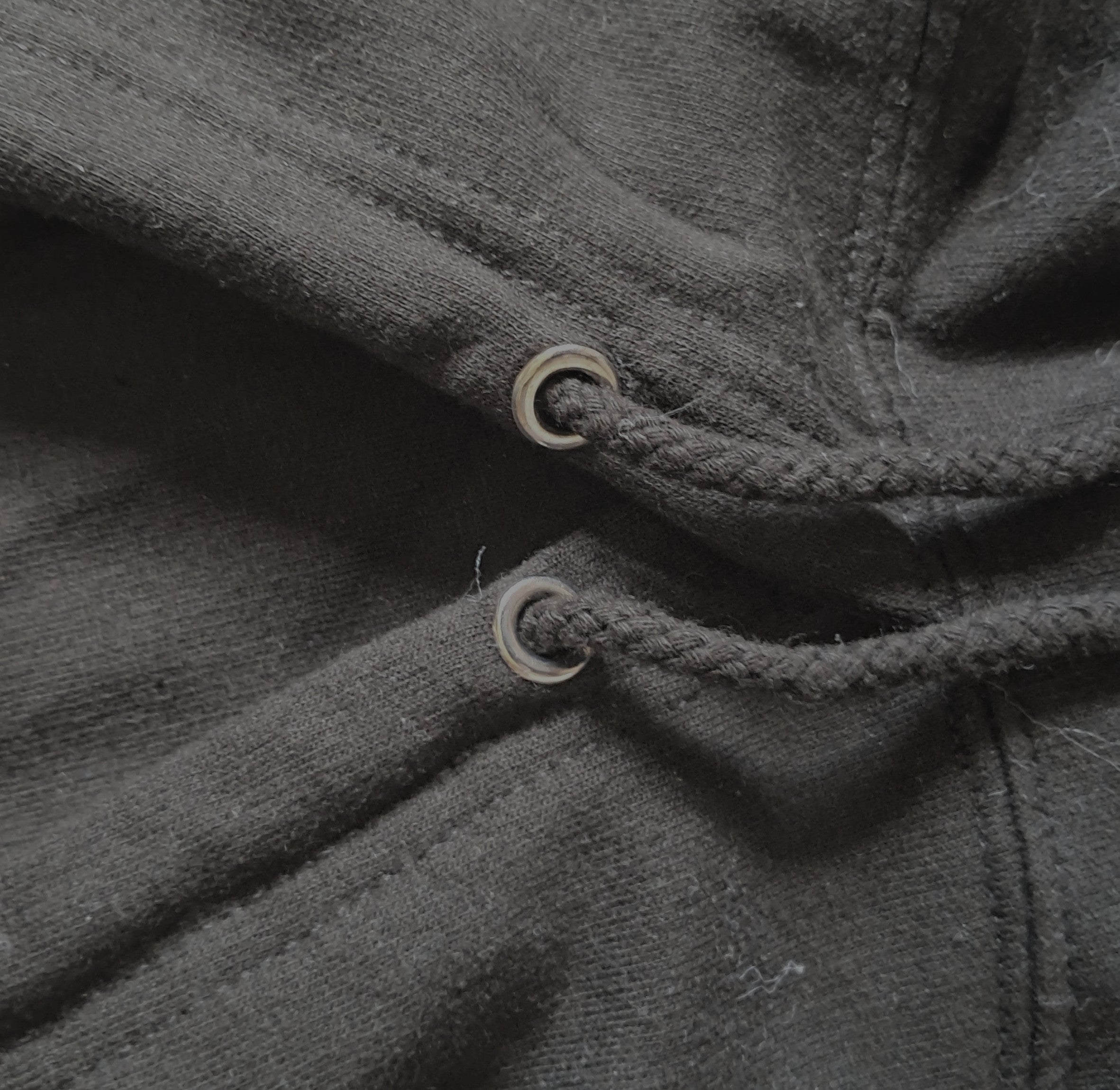 Close-up of a dark charcoal gray fabric garment showing a braided drawstring threaded through two metal eyelets promoting mental health and neurodivergence awareness by muted mayhem