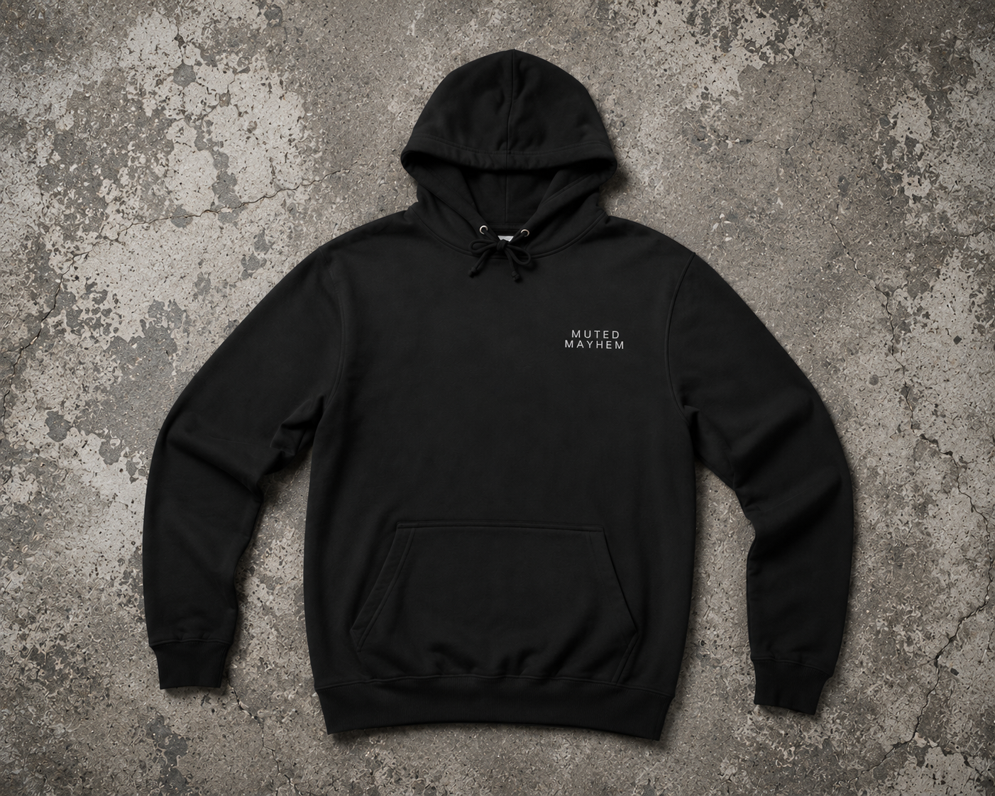 A black pullover hoodie with a small white 'MUTED MAYHEM' logo on the left chest, laid flat on a textured gray concrete background promoting mental health and neurodivergence awareness by muted mayhem