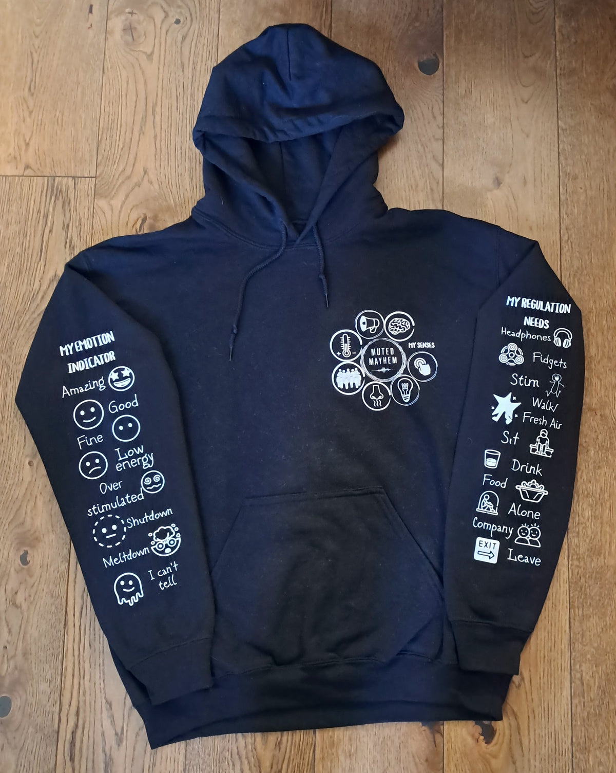 A navy blue pullover hoodie laid flat on a wooden floor, featuring white graphic text and illustrations printed on both sleeves and a central chest graphic.