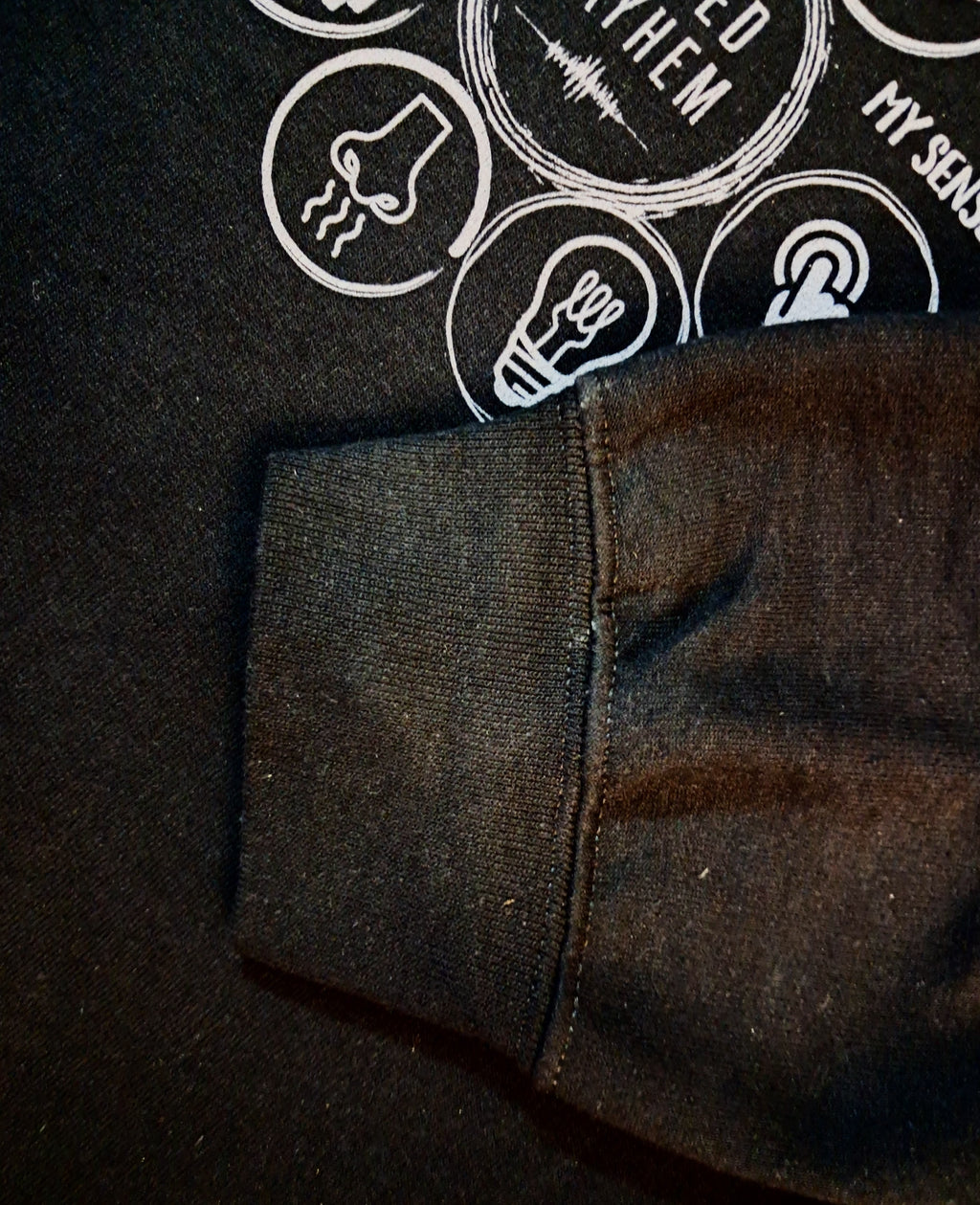 Close-up of a dark charcoal gray ribbed knit sleeve or cuff laid over a black graphic sweatshirt with white printed icons and text.