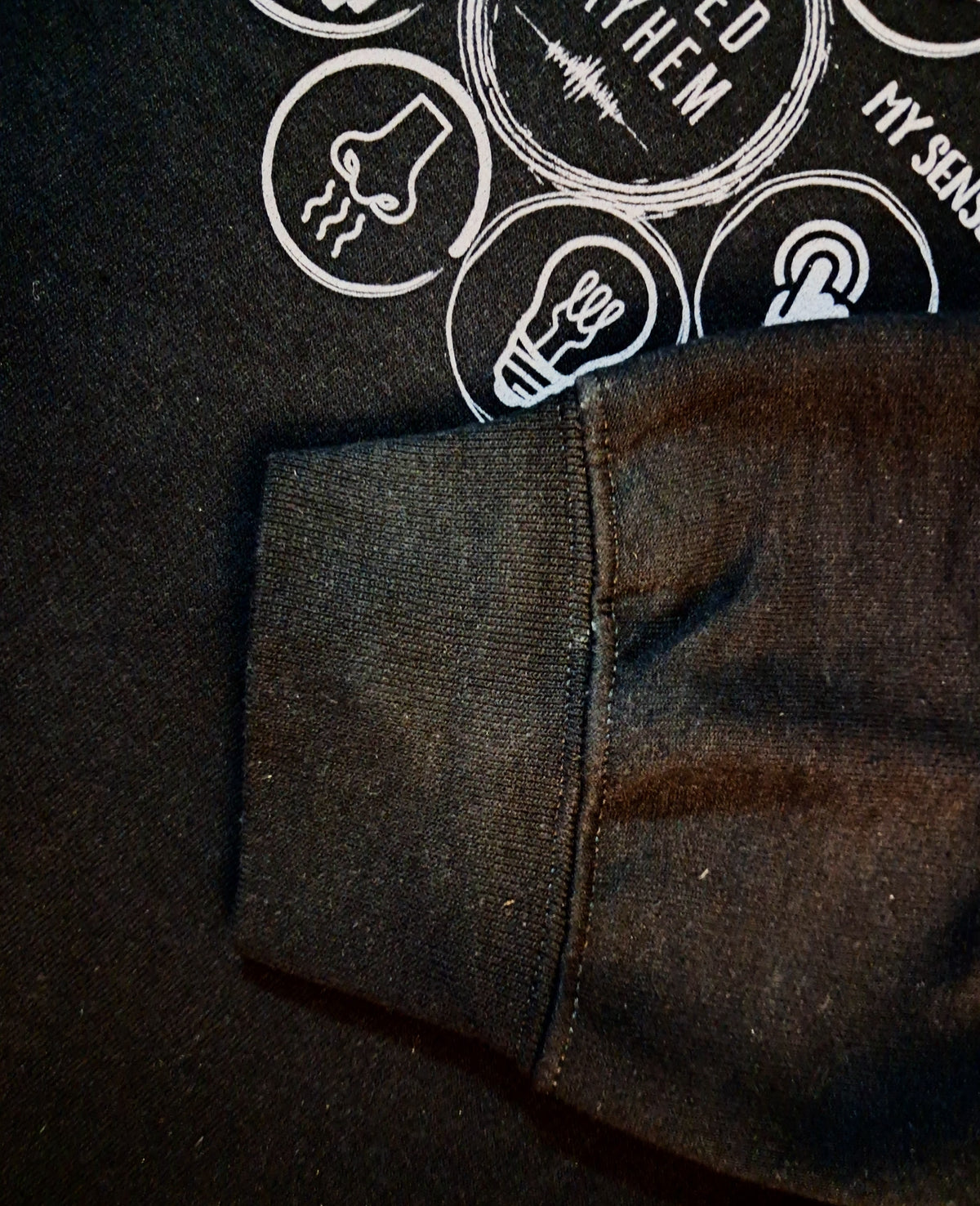 Close-up of a dark charcoal gray ribbed knit sleeve or cuff laid over a black graphic sweatshirt with white printed icons and text.