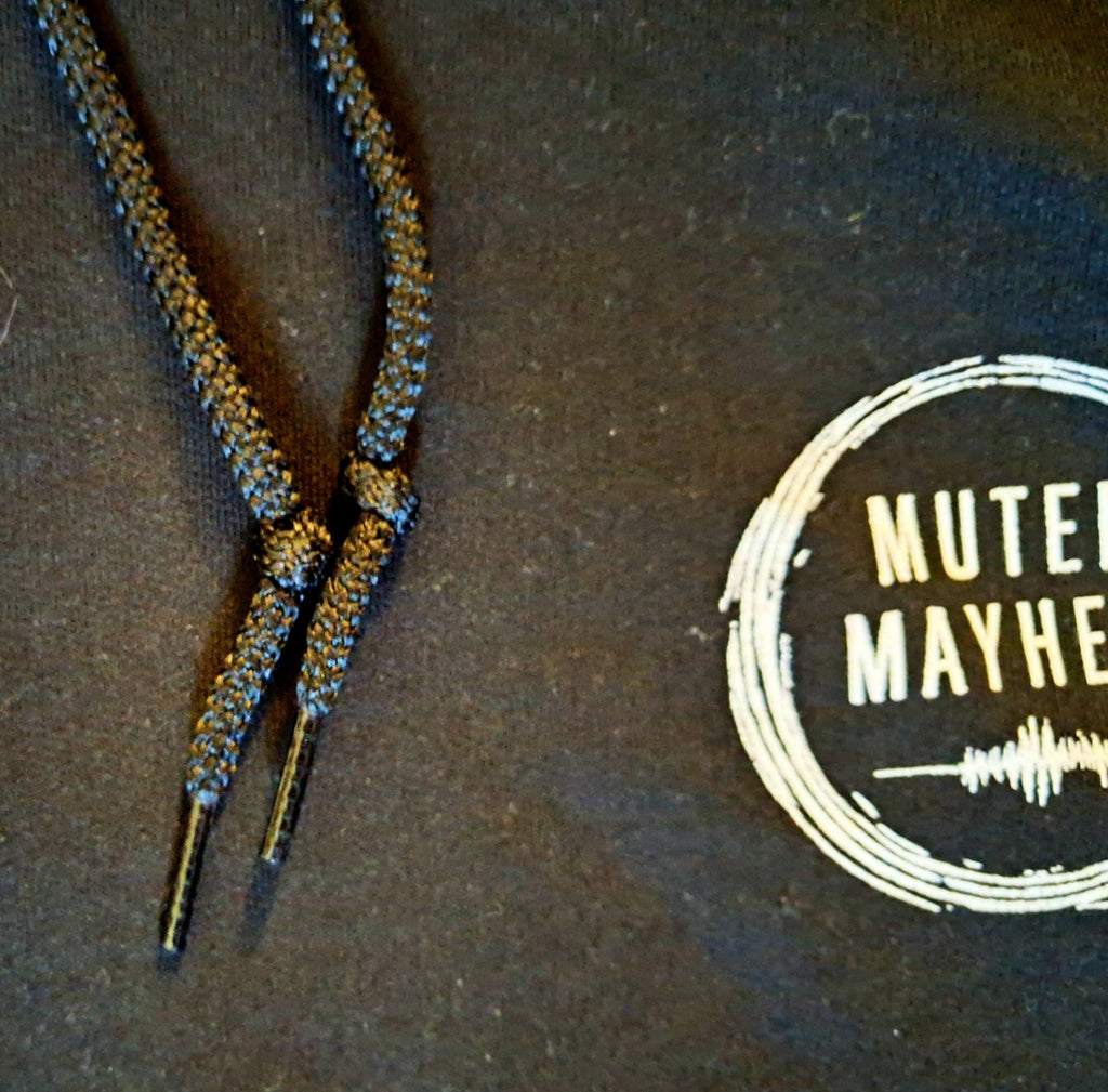 Close-up of black braided drawstrings threaded through metal eyelets on a dark charcoal hoodie, with a white distressed circular logo reading 'MUTED MAYHE' partially visible on the right.